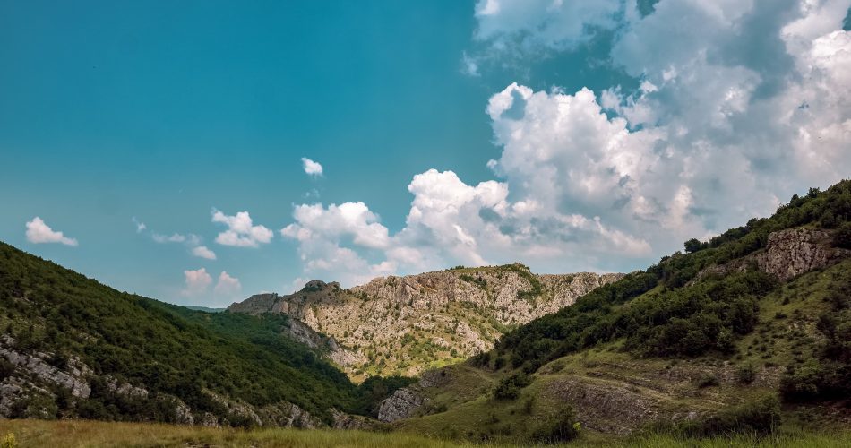 meadow surrounded by hills covered bushes trees cloudy sky sunlight 1